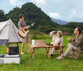 Three friends camping outdoors, with one playing guitar and a Jackery portable power station charging their laptop.